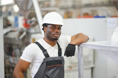 Endüstriyel mühendis portresi. Fabrika üretim hattında duran kasklı gülen fabrika işçisi..
