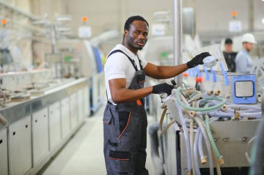 Afrikalı erkek mühendis, şirketin ürün işiyle ilgili plastik ve çelik endüstrisinde çalışarak, malzeme üretim makinesi sistemini kontrol etmek için makine dairesinde duruyor..