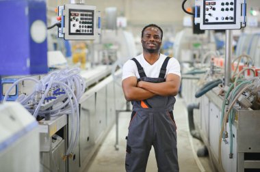 Afrikalı erkek mühendis, şirketin ürün işiyle ilgili plastik ve çelik endüstrisinde çalışarak, malzeme üretim makinesi sistemini kontrol etmek için makine dairesinde duruyor..