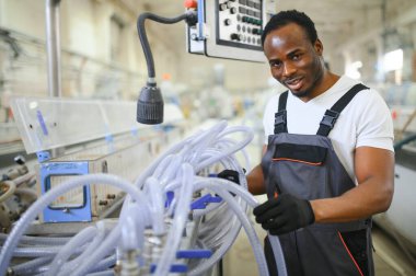 Afrikalı erkek mühendis, şirketin ürün işiyle ilgili plastik ve çelik endüstrisinde çalışarak, malzeme üretim makinesi sistemini kontrol etmek için makine dairesinde duruyor..
