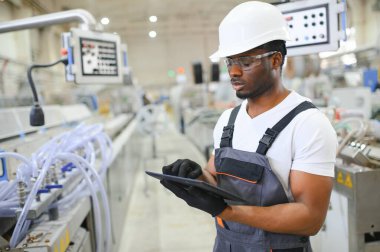 Endüstriyel mühendis portresi. Fabrika üretim hattında duran kasklı gülen fabrika işçisi..