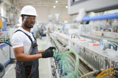 Endüstriyel mühendis portresi. Fabrika üretim hattında duran kasklı gülen fabrika işçisi..