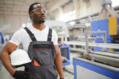 Endüstriyel mühendis portresi. Gülümseyen fabrika işçisi fabrika üretim hattında duruyor..