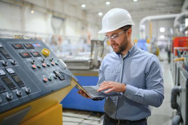 Sert şapkalı mühendis ağır bir sanayi fabrikasında dizüstü bilgisayar kullanıyor..