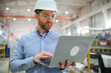 Sert şapkalı mühendis ağır bir sanayi fabrikasında dizüstü bilgisayar kullanıyor..