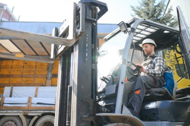 Forklift kullanan bir adam büyük bir depoda çalışır ve bir çanta dolusu hammaddeyi boşaltır..