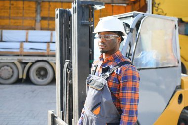 Afro-Amerikan Adam iş başında. Profesyonel operasyon mühendisliği. Genç işçi forklift sürücüsü.