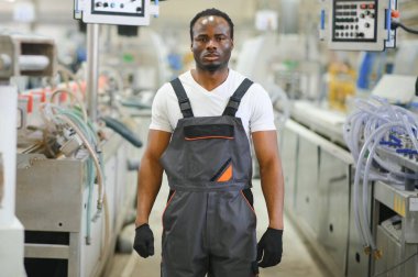 Üniformalı ve endüstriyel fabrikada ayakta duran Afrikalı Amerikalı erkek mühendisin portresi.