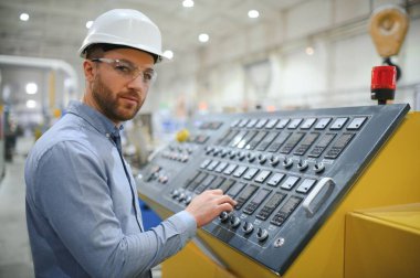 Sert şapkalı mühendis ağır bir sanayi fabrikasında dizüstü bilgisayar kullanıyor..