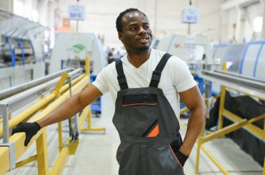 Endüstriyel mühendis portresi. Gülümseyen fabrika işçisi fabrika üretim hattında duruyor..