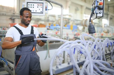Afrikalı erkek mühendis, şirketin ürün işiyle ilgili plastik ve çelik endüstrisinde çalışarak, malzeme üretim makinesi sistemini kontrol etmek için makine dairesinde duruyor..