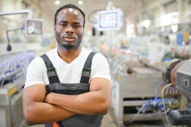 Afrikalı erkek mühendis, şirketin ürün işiyle ilgili plastik ve çelik endüstrisinde çalışarak, malzeme üretim makinesi sistemini kontrol etmek için makine dairesinde duruyor..