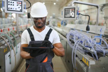 Endüstriyel mühendis portresi. Fabrika üretim hattında duran kasklı gülen fabrika işçisi..