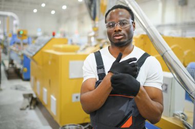 Afrikalı erkek mühendis, şirketin ürün işiyle ilgili plastik ve çelik endüstrisinde çalışarak, malzeme üretim makinesi sistemini kontrol etmek için makine dairesinde duruyor..