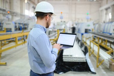 Genç bir erkek mühendis plastik pencere çerçevelerinin üretimini denetliyor.