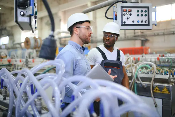 Two Diverse Professional Heavy Industry Engineers Wearing Safety Uniform and Hard Hats Working on Laptop.