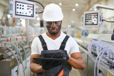 Afrikalı erkek mühendis, şirketin ürün işiyle ilgili plastik ve çelik endüstrisinde çalışarak, malzeme üretim makinesi sistemini kontrol etmek için makine dairesinde duruyor..