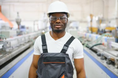 Endüstriyel mühendis portresi. Fabrika üretim hattında duran kasklı gülen fabrika işçisi..