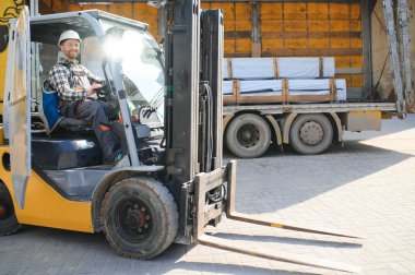 Forklift kullanan bir adam büyük bir depoda çalışır ve bir çanta dolusu hammaddeyi boşaltır..