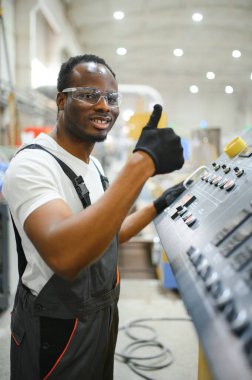 Afrikalı erkek mühendis, şirketin ürün işiyle ilgili plastik ve çelik endüstrisinde çalışarak, malzeme üretim makinesi sistemini kontrol etmek için makine dairesinde duruyor..