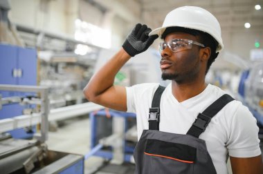 Afrikalı erkek mühendis, şirketin ürün işiyle ilgili plastik ve çelik endüstrisinde çalışarak, malzeme üretim makinesi sistemini kontrol etmek için makine dairesinde duruyor..