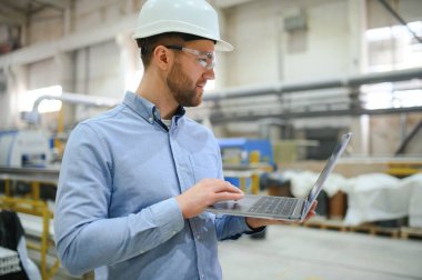 Genç bir erkek mühendis plastik pencere çerçevelerinin üretimini denetliyor.