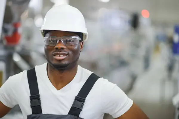 Portrait of African American male engineer in uniform and standing in industrial factory.