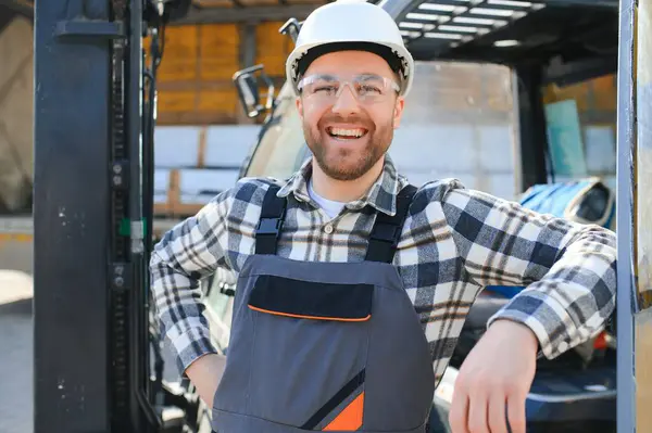 forklift driver in protective vest and forklift standing at warehouse of freight forwarding company, smiling.