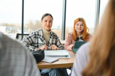 Öğrenciler ortak masada oturup üniversitede birlikte ders çalışırken notlar alıyorlar..