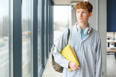 Gülümseyen, kıvırcık saçlı, elinde kitapla kameraya bakan bir gencin portresi. Okula dönüş, eğitim konsepti..