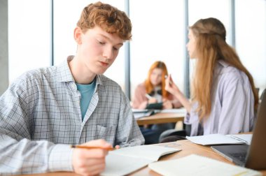 Test. Üst üste oturan ve test kitaplarında sınava sahip genç öğrencilerin yakın çekim.