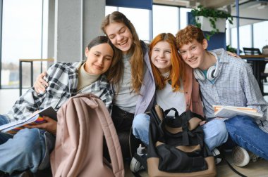 Bir grup neşeli öğrenci bir sınıfta yerde oturuyorlar..