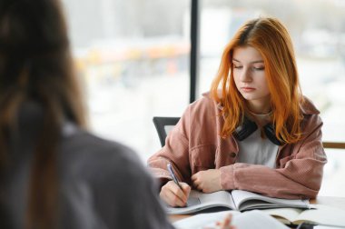 Öğrenciler ortak masada oturup üniversitede birlikte ders çalışırken notlar alıyorlar..