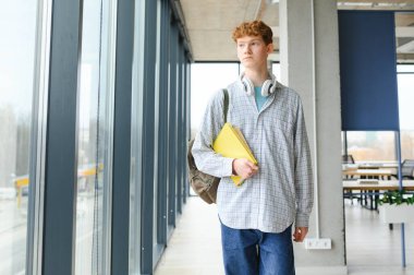 Sırt çantalı genç bir üniversite öğrencisi üniversitenin koridorunda duruyor..
