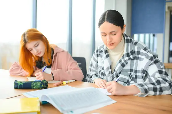 stock image students sit at shared desk making notes studying together at university.
