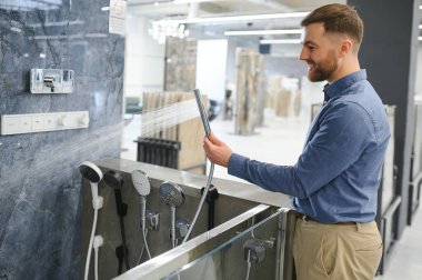 Bir duş musluğu seçiyor. Adam hijyenik eşya dükkanından ürün seçiyor..