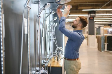 Bir duş musluğu seçiyor. Adam hijyenik eşya dükkanından ürün seçiyor..