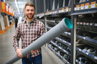 male plumber in a hardware store chooses the sewer pipes, the concept of plumbing work in the house.