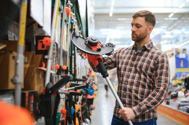 Bahçe malzemeleri dükkanındaki genç bir adam çim biçmek için elektrikli budama makinesi seçiyor..