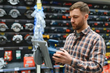 Hırdavatçıdaki bir adam yeni bir yörünge zımpara makinesi seçer..