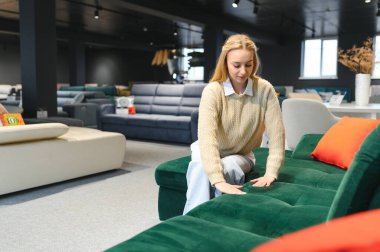 Mutlu genç bir kadın mobilya mağazasında kanepe seçiyor..