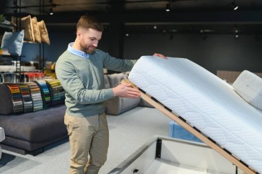 Mobilya mağazasında satışta olan ortopedik yatağı inceleyen genç bir erkek müşteri..