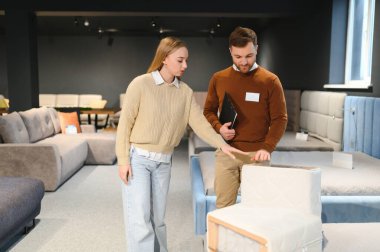 Genç satıcı, müşteriye yeni modern kanepe seçmesinde yardımcı oluyor..