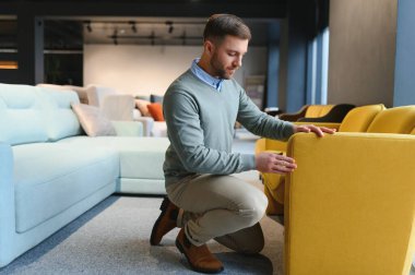 Mobilya mağazasında sandalyeyi seçen müşterinin ön görüntüsü. Yakışıklı, esmer, sakallı, ayakta duran, dokunan, aşağı bakan, satın alan bir erkek. Alışveriş ve modern yaşam tarzı kavramı.