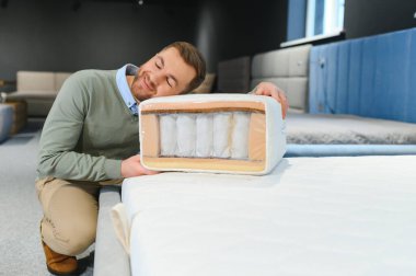 Mobilya mağazasında satışta olan ortopedik yatağı inceleyen genç bir erkek müşteri..