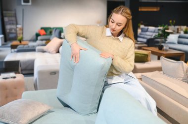 Mutlu genç bir kadın mobilya mağazasında kanepe seçiyor..
