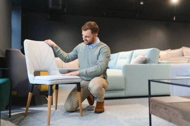 Mobilya mağazasında sandalyeyi seçen müşterinin ön görüntüsü. Yakışıklı, esmer, sakallı, ayakta duran, dokunan, aşağı bakan, satın alan bir erkek. Alışveriş ve modern yaşam tarzı kavramı.