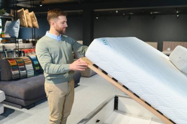 Mobilya mağazasında satışta olan ortopedik yatağı inceleyen genç bir erkek müşteri..