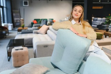 Mutlu genç bir kadın mobilya mağazasında kanepe seçiyor..