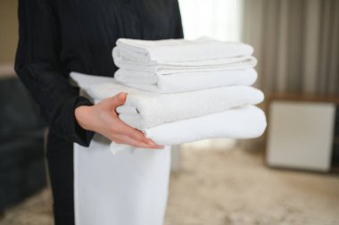 Kadın oda hizmetçisi temiz beyaz havlular tutuyor..